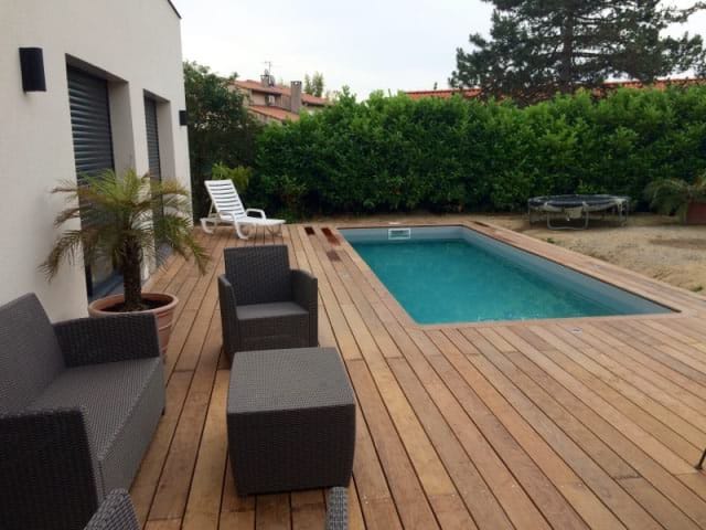 Terrasse en bois exotique autour d'une piscine rectangulaire avec salon de jardin en rotin et palmier en pot près de la maison.