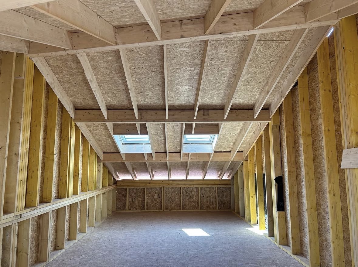 Charpente bois d'un grenier en rénovation avec panneaux OSB et deux fenêtres de toit lumineuses.