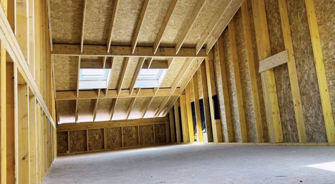 Charpente bois apparente avec fenêtres de toit dans des combles en cours de construction.