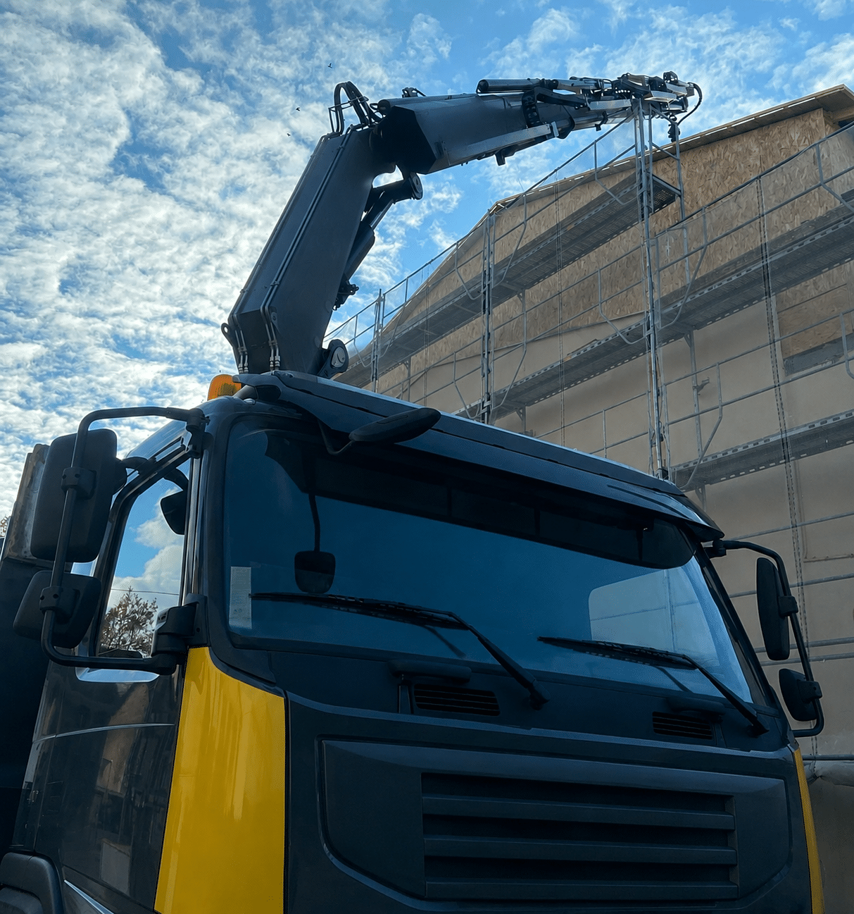Camion grue jaune et noir devant un immeuble en chantier avec échafaudages.