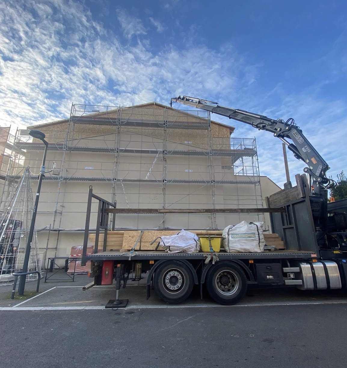 Camion grue Fassi devant un échafaudage de chantier de rénovation avec sacs Castorama.