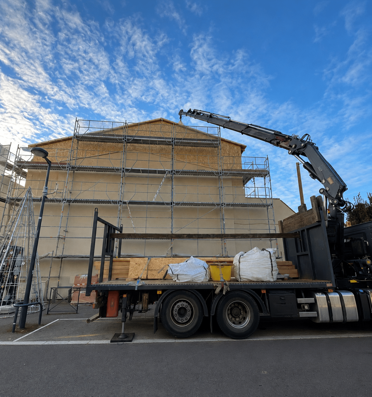 Camion-grue sur chantier avec échafaudage et bâtiment en rénovation sous ciel bleu.