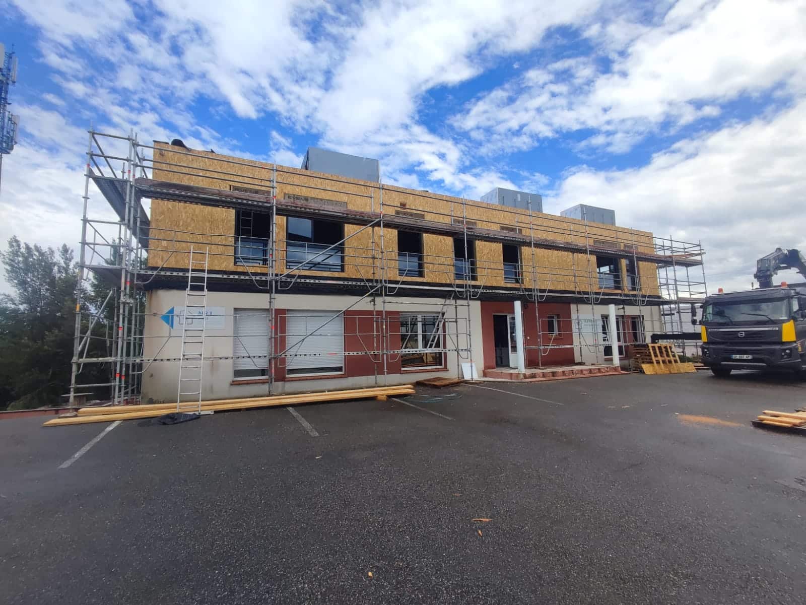 Bâtiment en rénovation avec échafaudage, extension en bois OSB et camion sur un chantier.