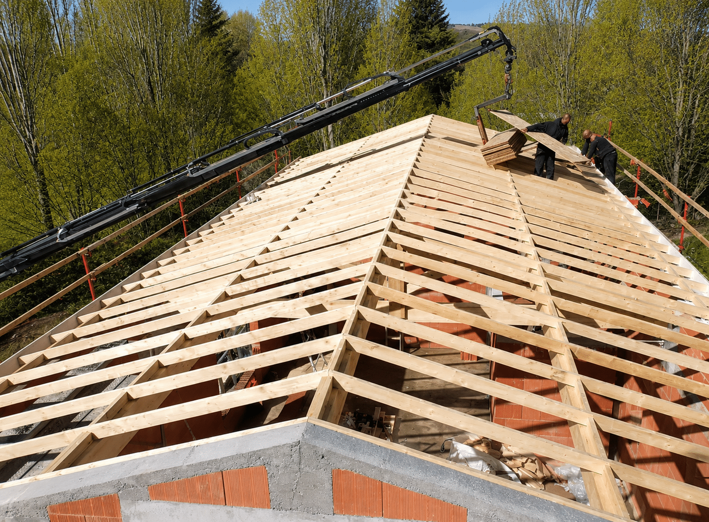 Charpente bois en construction avec grue livrant des panneaux et ouvriers sur le toit d'une maison.