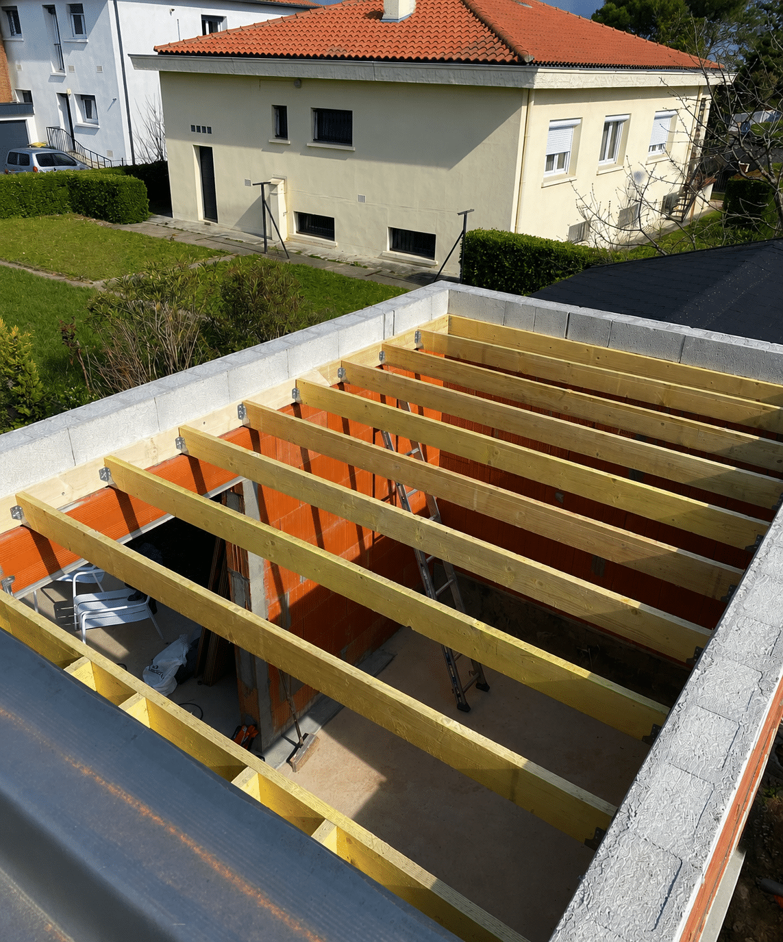 Solives de toit en bois installées sur une structure en briques et parpaings pour une extension de maison.