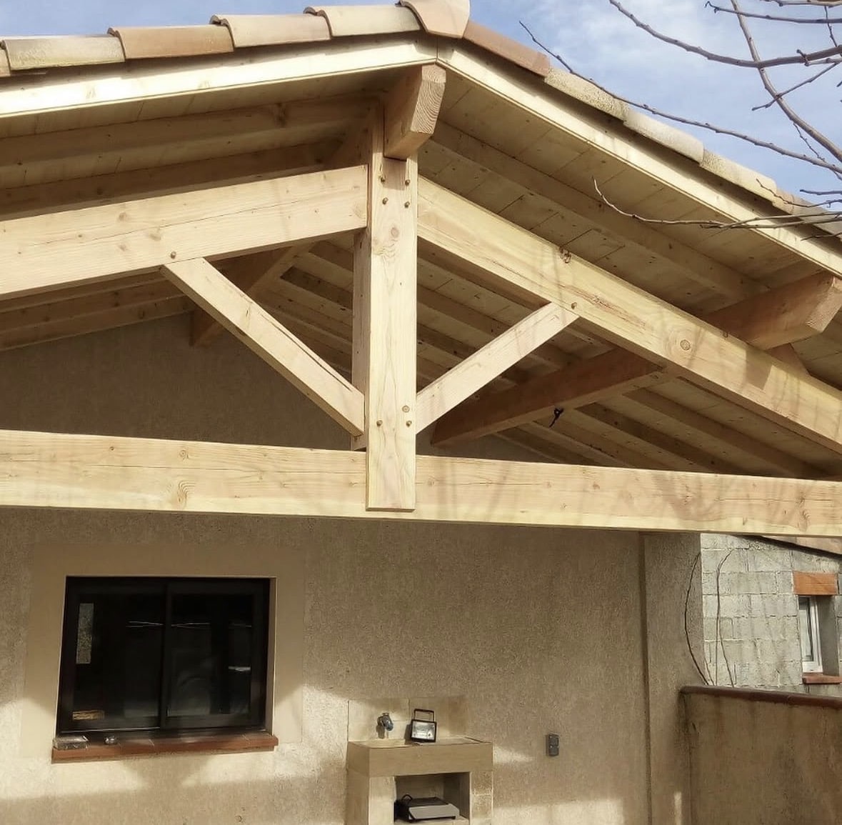 Charpente bois traditionnelle avec ferme à poinçon pour terrasse couverte et toiture en tuiles.
