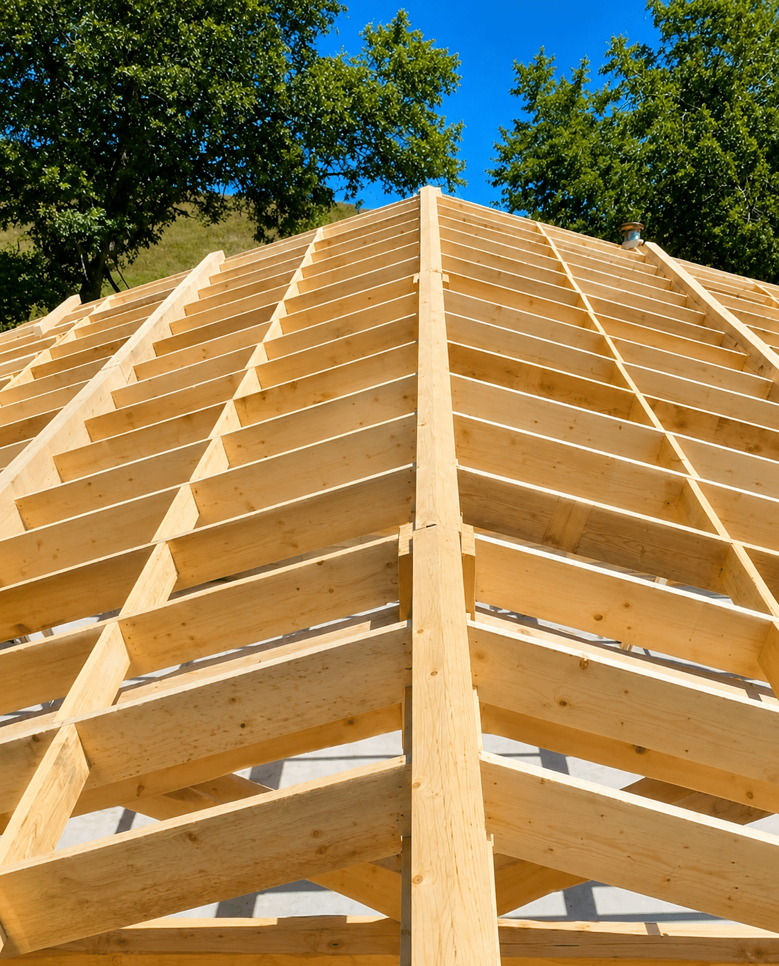 Charpente de toit en bois clair sous un ciel bleu, structure de maison neuve avec vue en perspective.