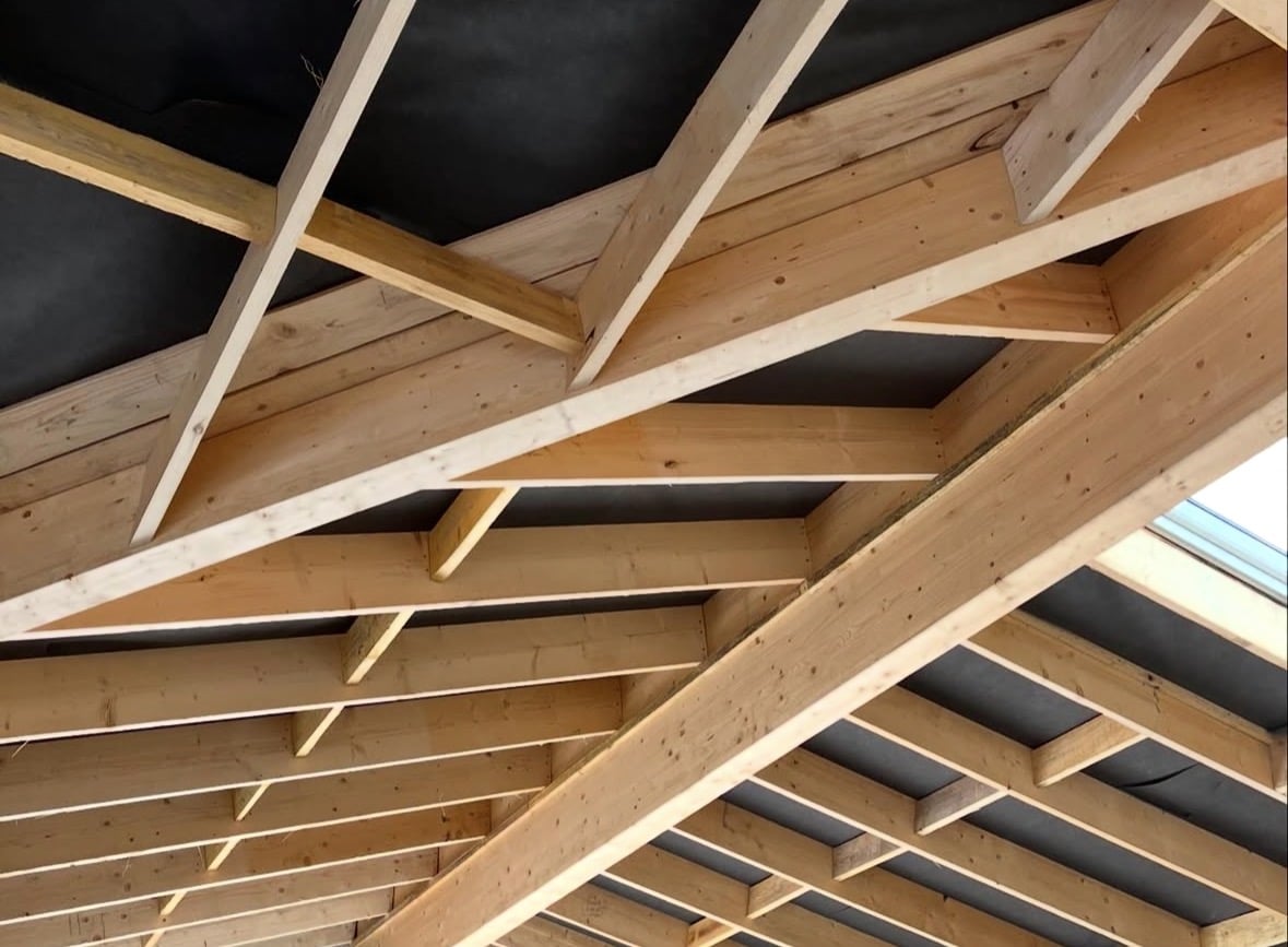 Charpente bois apparente, chevrons et membrane noire sous toiture en construction.