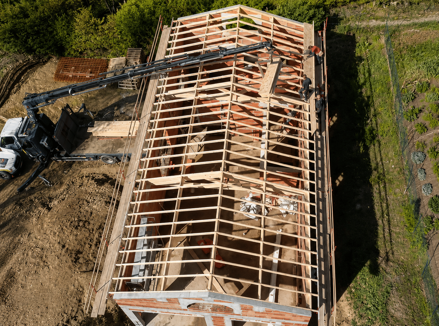 Grue levant du bois sur une charpente de maison en construction avec ouvriers actifs sur le toit.