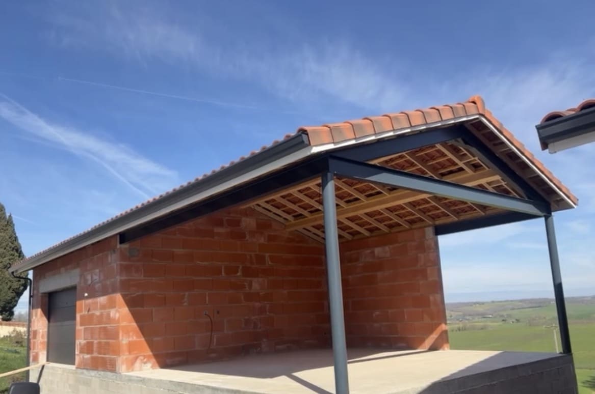 Construction d'un garage en briques rouges avec charpente métallique anthracite et toiture en tuiles.