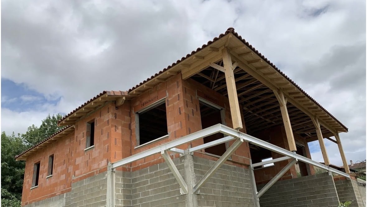 Maison en briques bio'bric en construction avec charpente bois, tuiles rouges et structure métallique de terrasse.