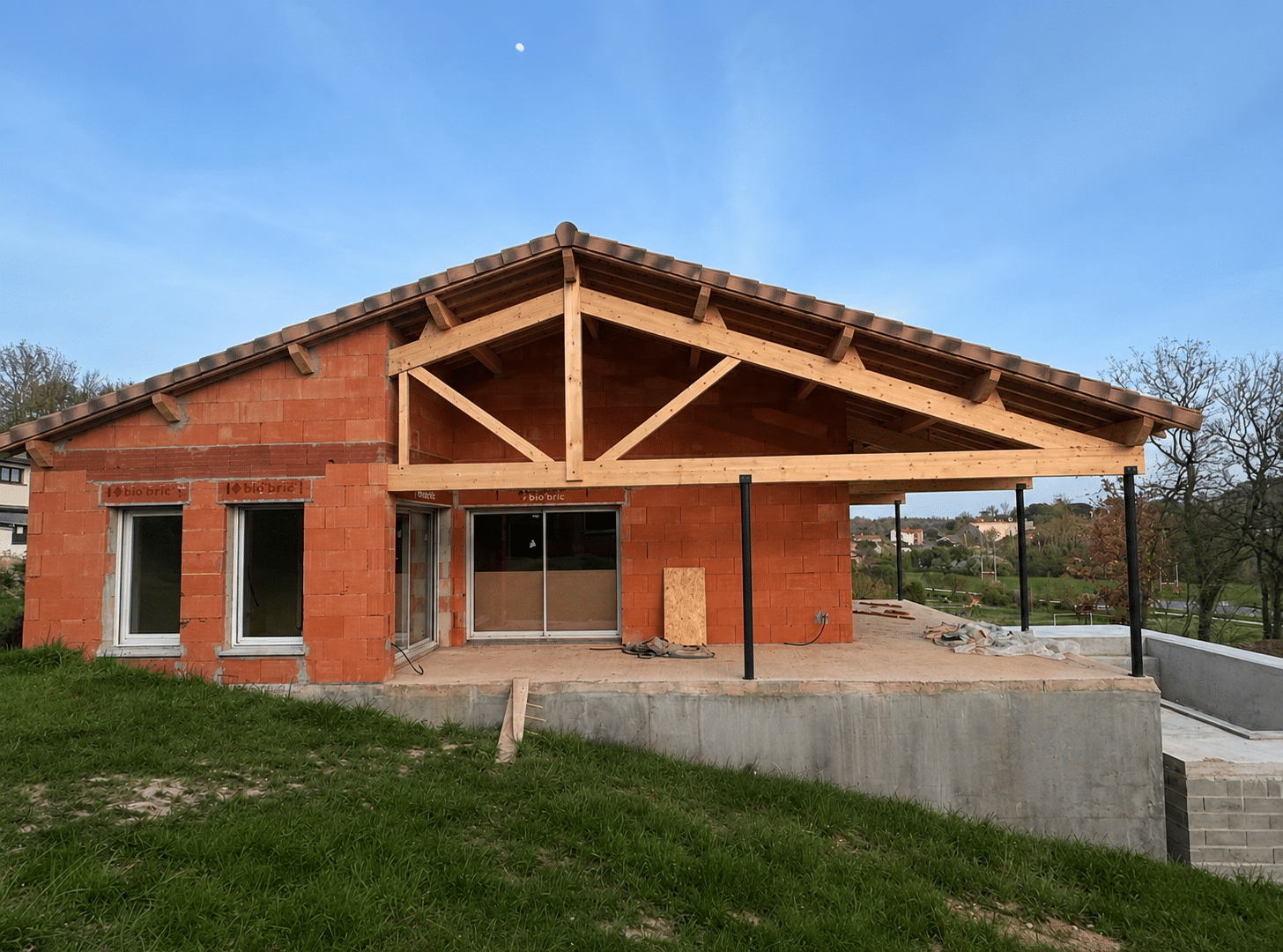 Maison en briques rouges bio'bric avec charpente bois et terrasse sur fondations en béton.