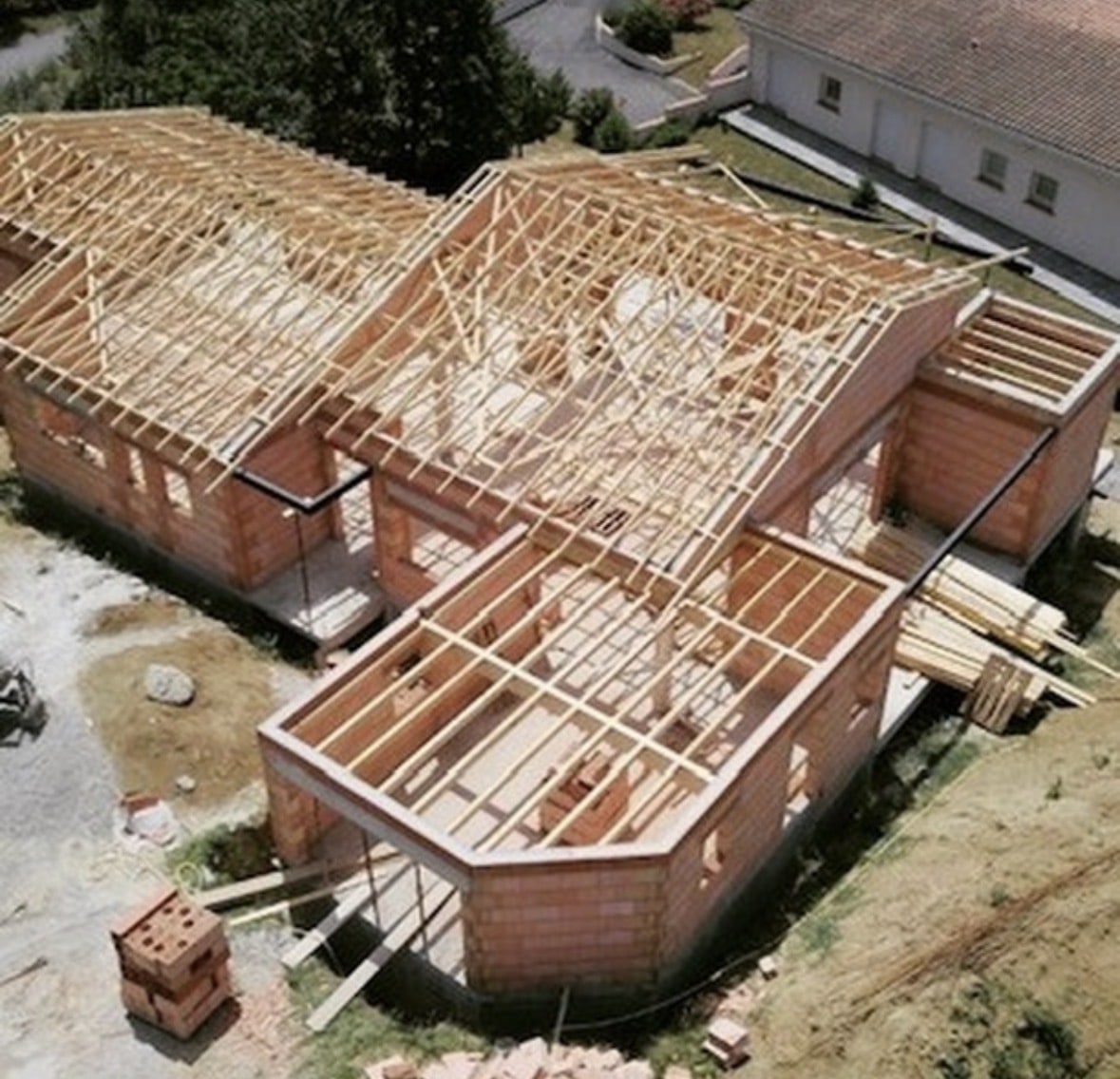 Maison en briques avec charpente bois apparente en cours de construction sur un chantier.