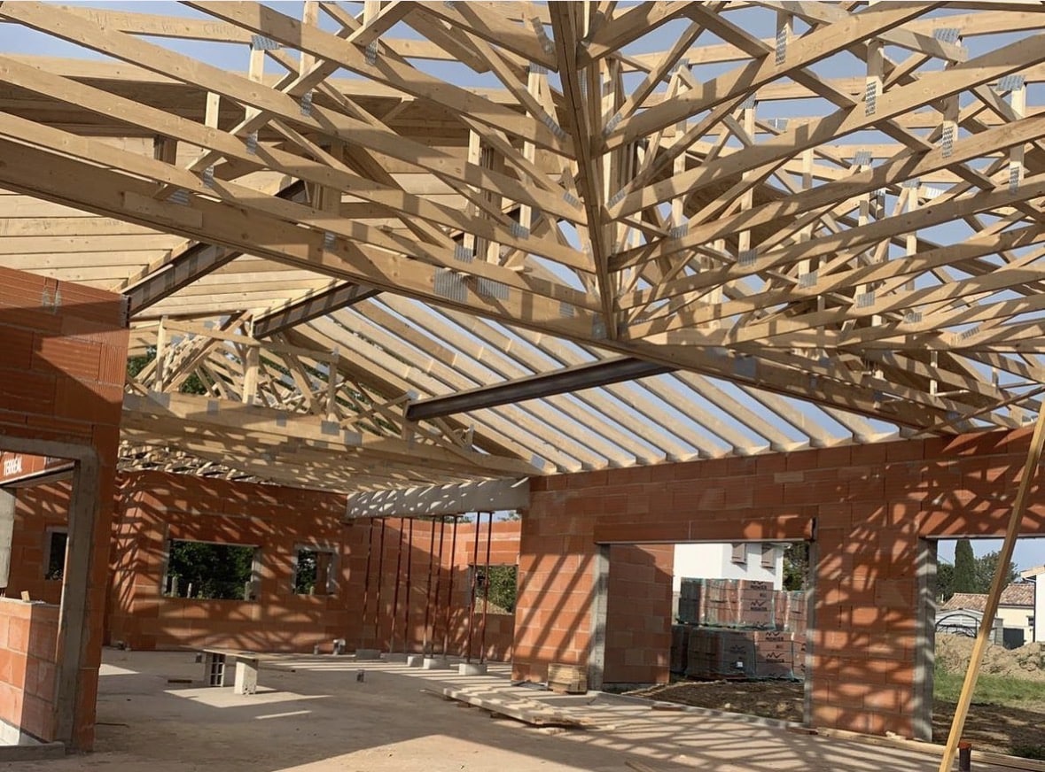 Charpente bois complexe et murs en briques d'une maison individuelle en construction.