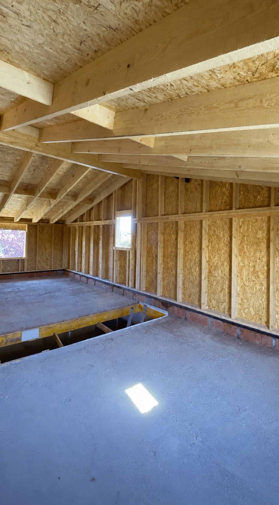Intérieur d'une construction en ossature bois avec murs OSB, charpente apparente et dalle béton.