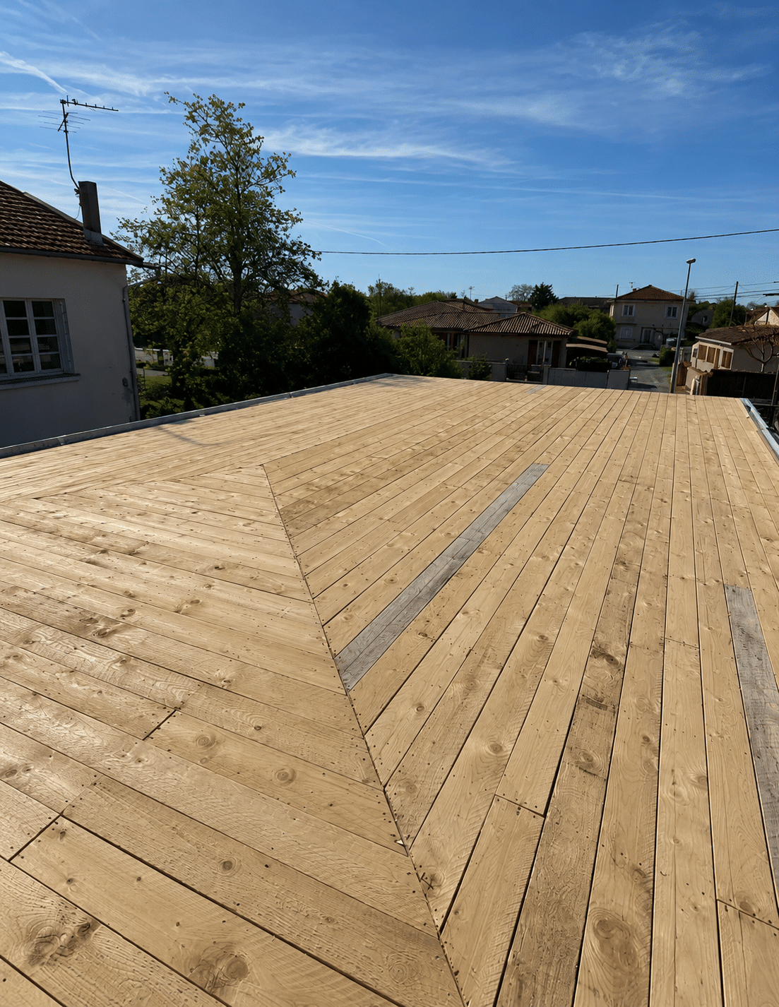 Toit-terrasse en bois clair aux planches géométriques sous un ciel bleu en zone résidentielle.