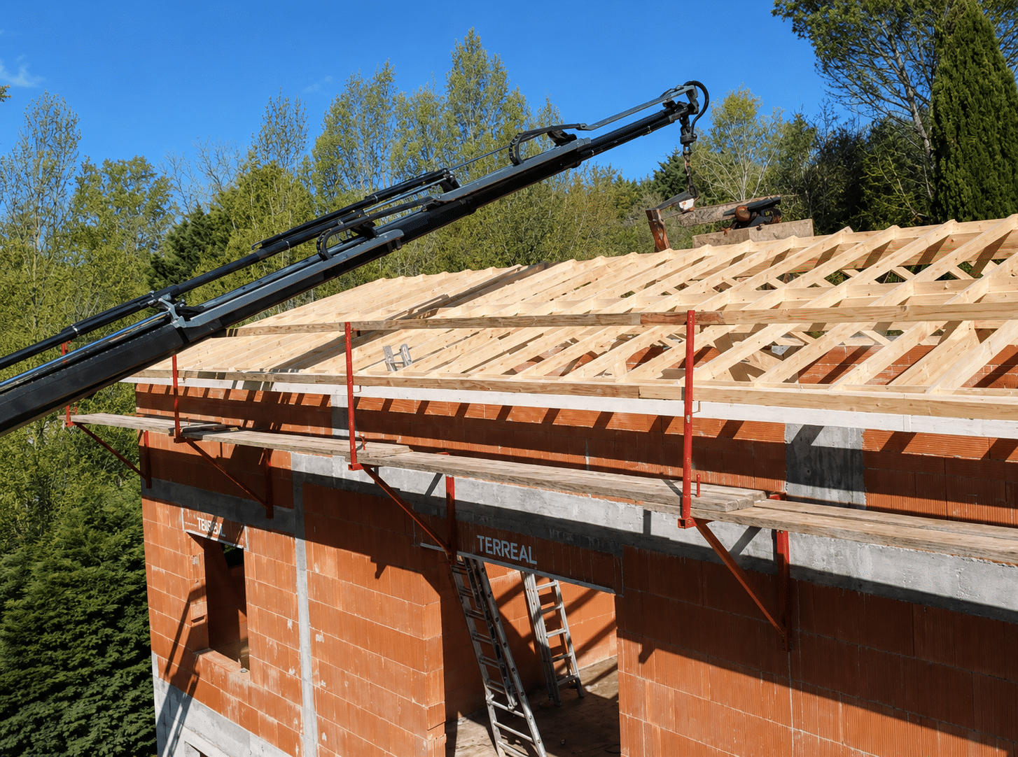 Chantier de toiture en bois sur briques Terreal avec grue télescopique et échafaudage.