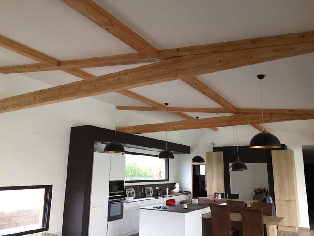 Cuisine moderne à plafond cathédrale avec poutres en bois croisées et suspensions noires.