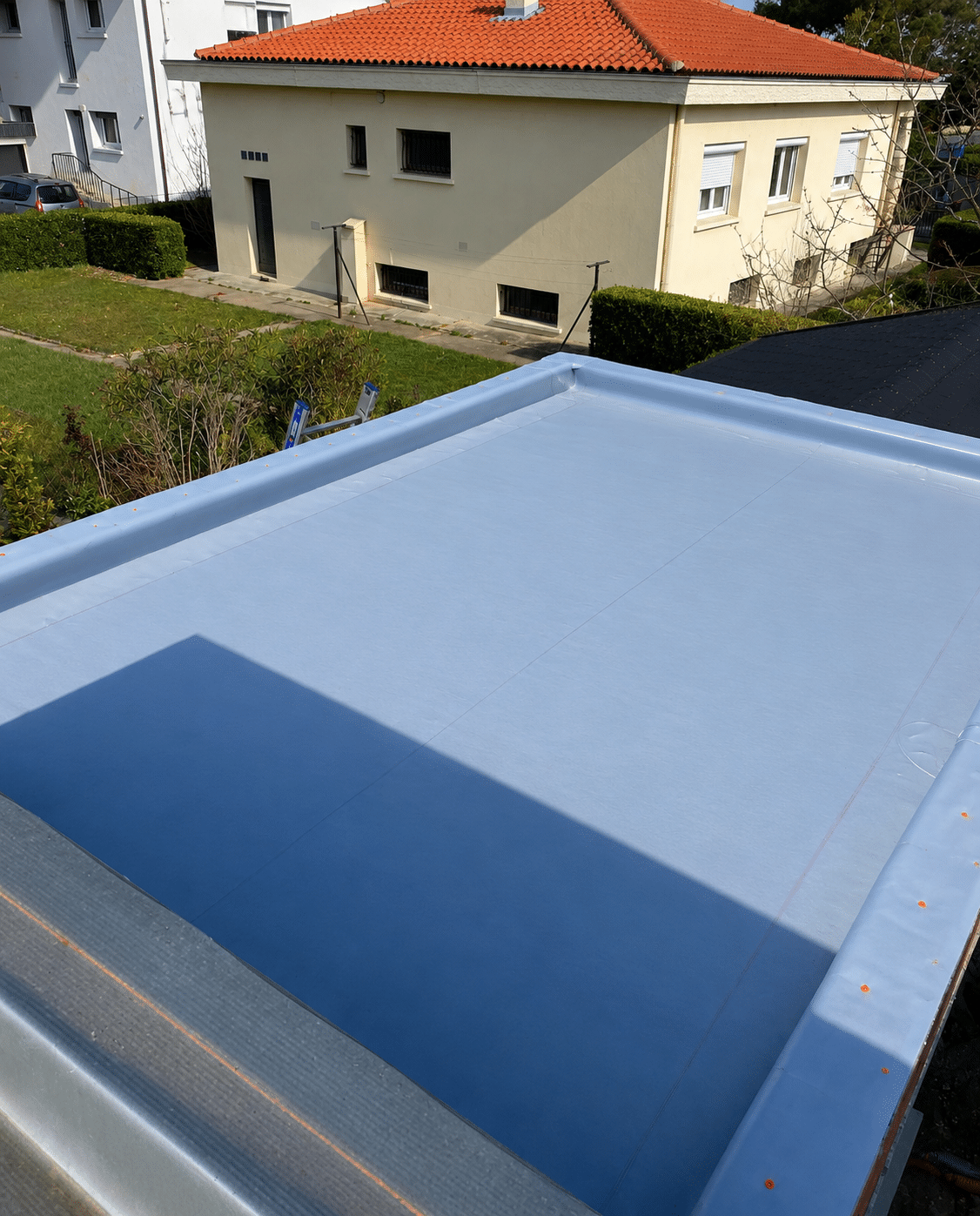 Membrane d'étanchéité bleu clair sur toiture terrasse devant une maison résidentielle.