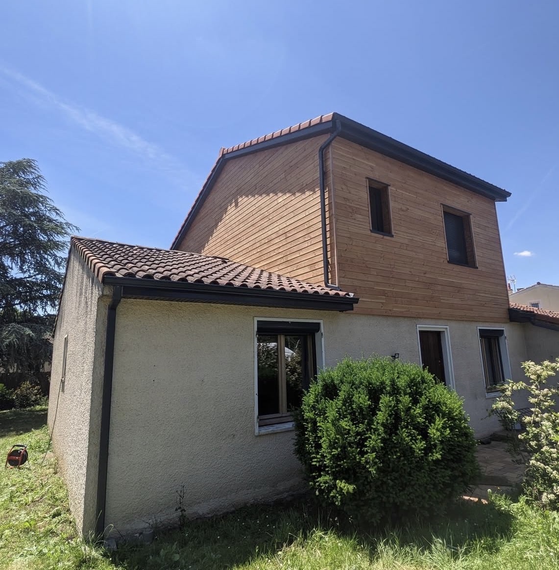 Maison avec extension en bardage bois et façade beige.