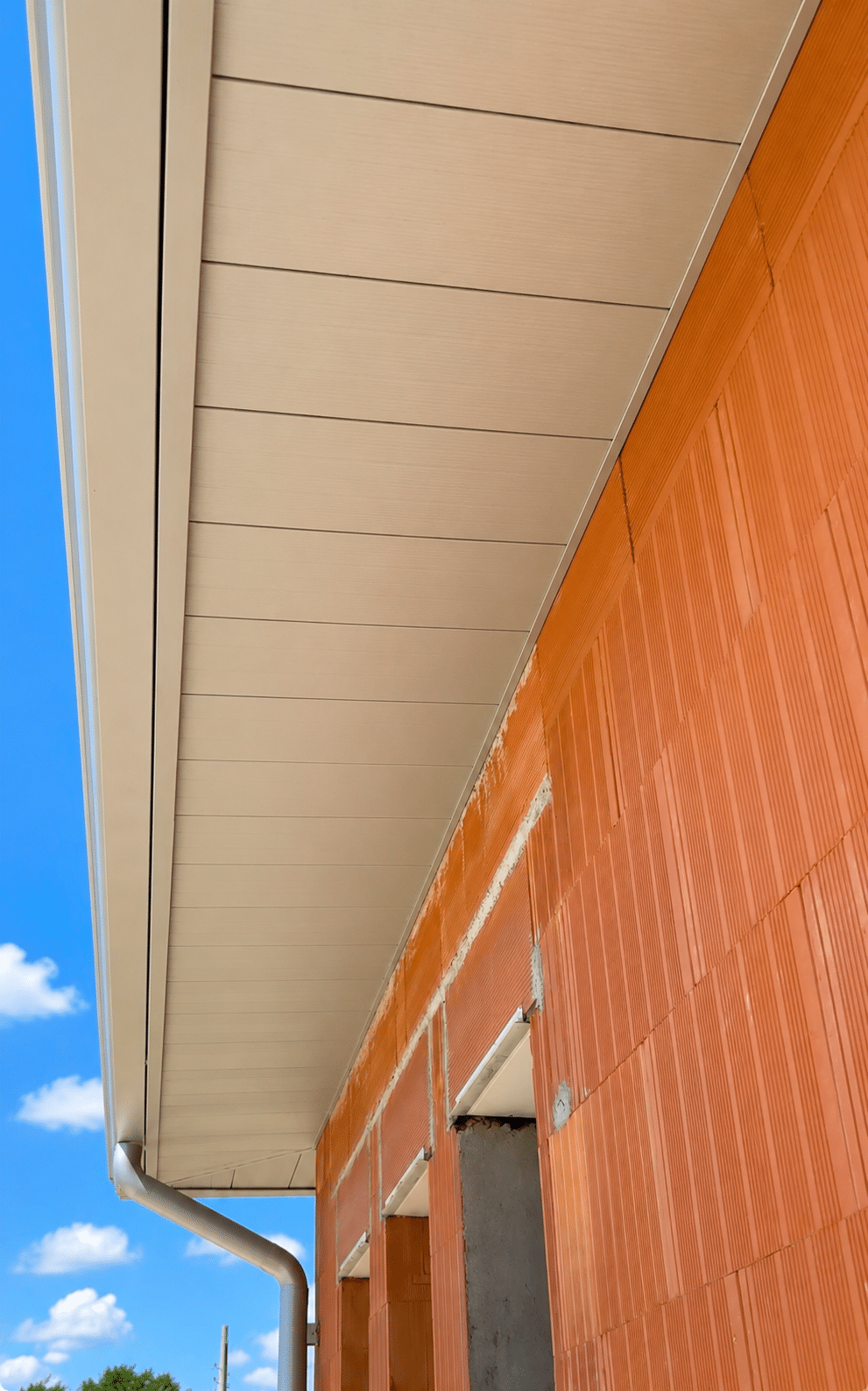Habillage de sous-toiture beige sur mur en briques, chantier de construction.