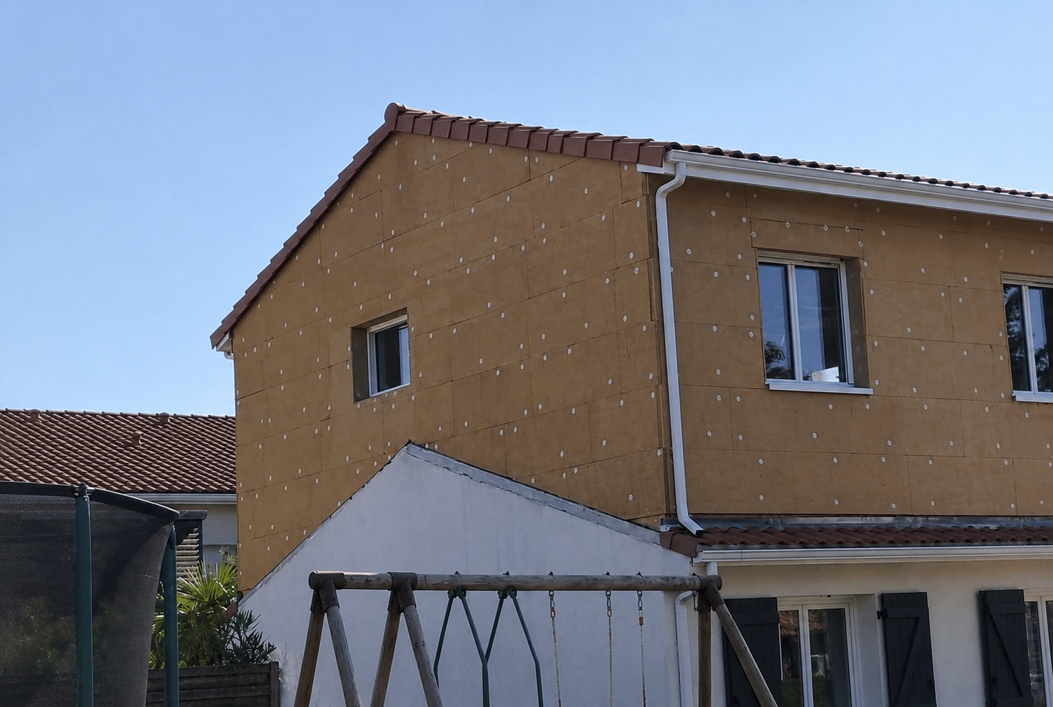 Maison en rénovation avec isolation thermique extérieure par panneaux bruns et fixations sous un ciel bleu.
