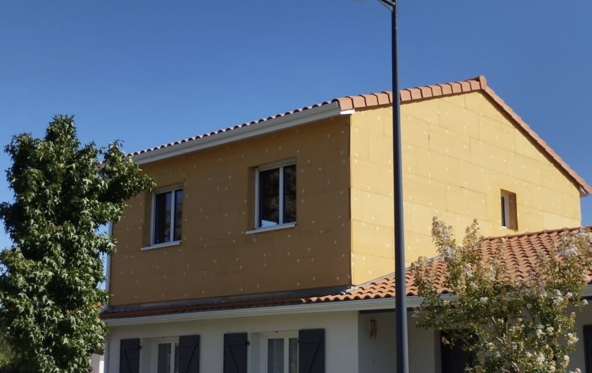 Isolation thermique par l'extérieur avec panneaux jaunes sur une façade de maison individuelle sous un toit de tuiles.