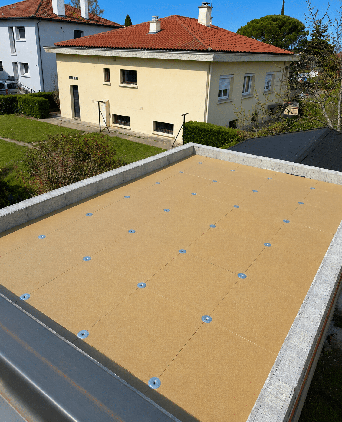 Isolation de toit plat : panneaux rigides jaunes fixés par rondelles métalliques sur structure en béton.