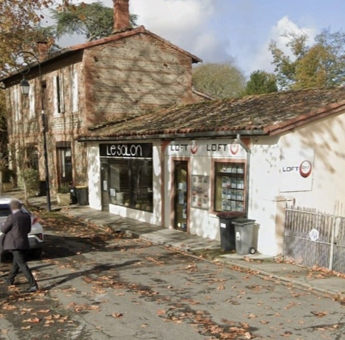 Façade des enseignes Le Salon et Loft One, rue pavée de feuilles d'automne avec un passant.