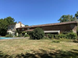 Longère en briques avec piscine et jardin sous un ciel bleu dégagé.