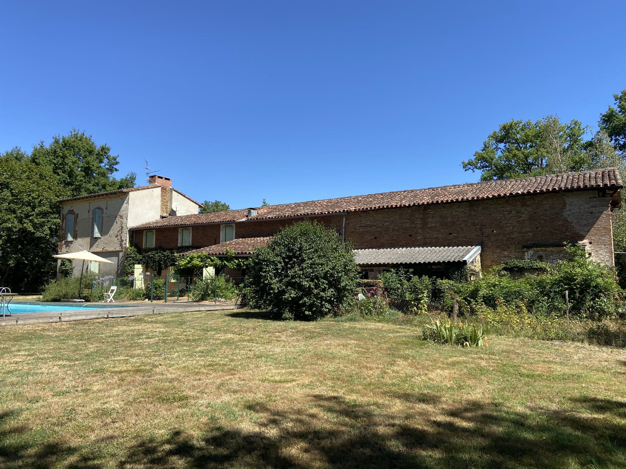 Longère en briques avec piscine et jardin sous un ciel bleu dégagé.