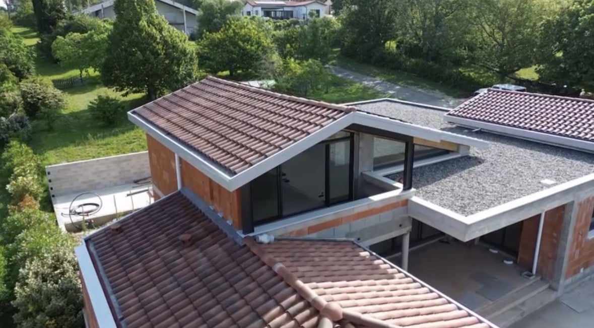 Maison moderne en briques avec toits en tuiles rouges, toit-terrasse en gravier et grandes baies vitrées.
