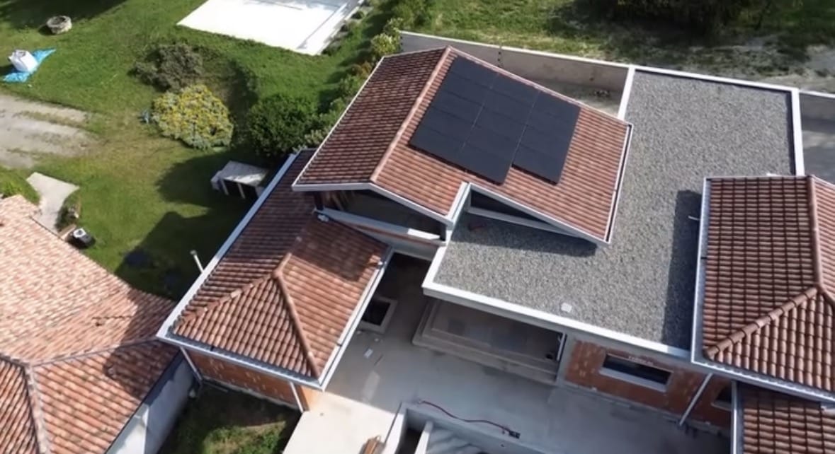 Vue aérienne d'une maison avec toiture en tuiles rouges et panneaux solaires noirs installés.