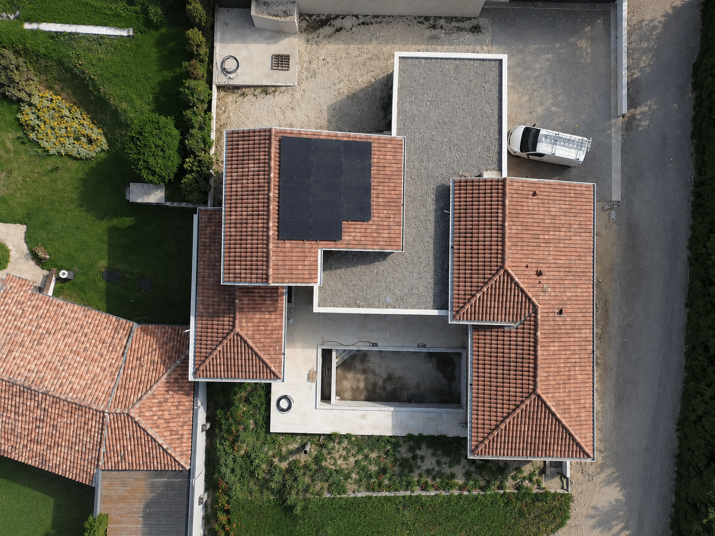 Vue aérienne d'une toiture en tuiles rouges avec panneaux solaires et piscine vide.