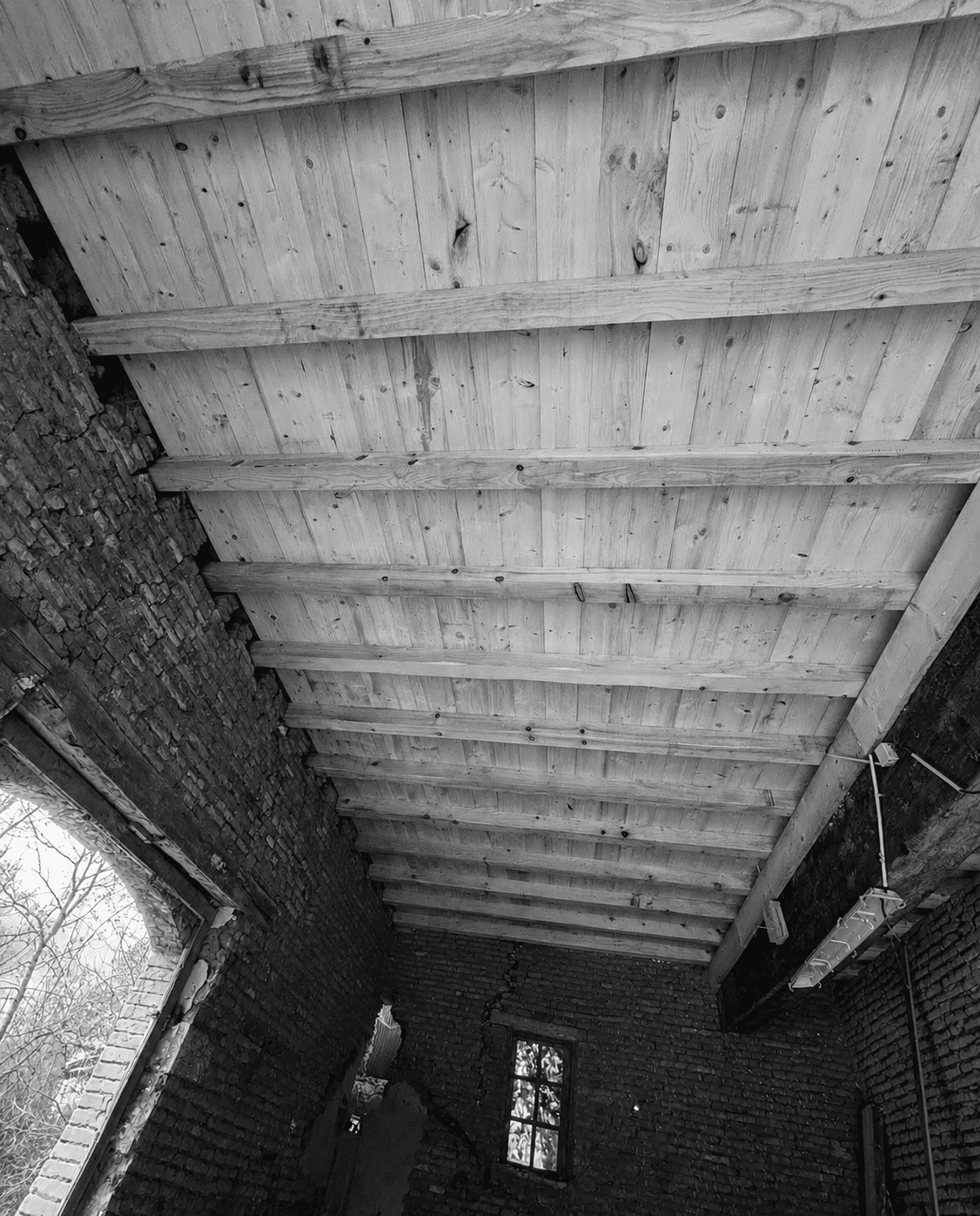 Intérieur rustique en noir et blanc montrant un plafond à poutres de bois et des murs de briques anciennes.