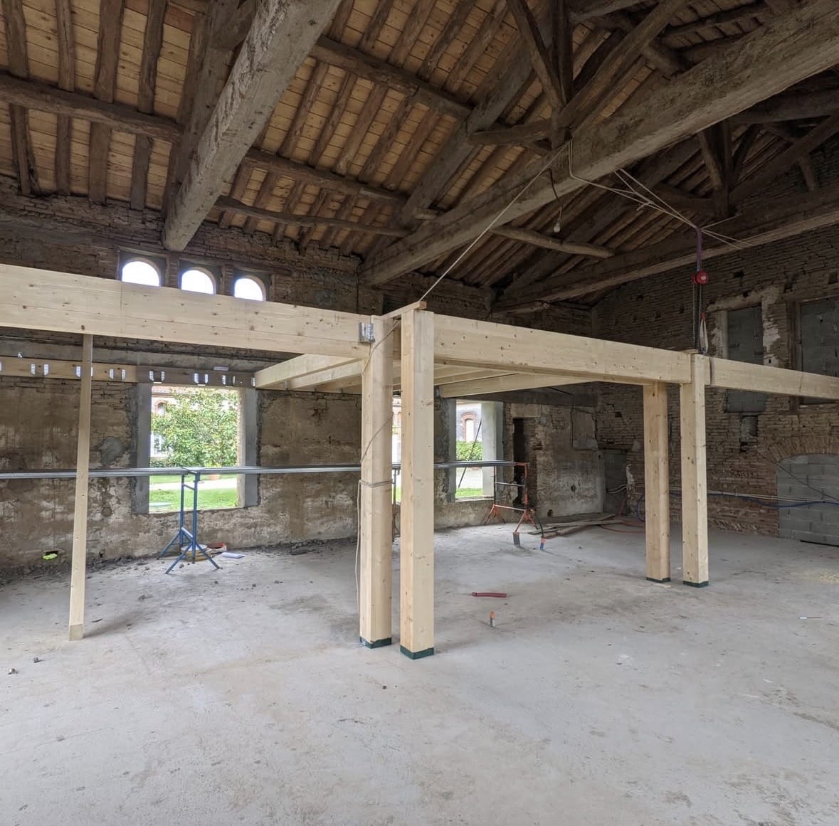 Structure bois neuve dans bâtiment ancien en briques avec charpente apparente.