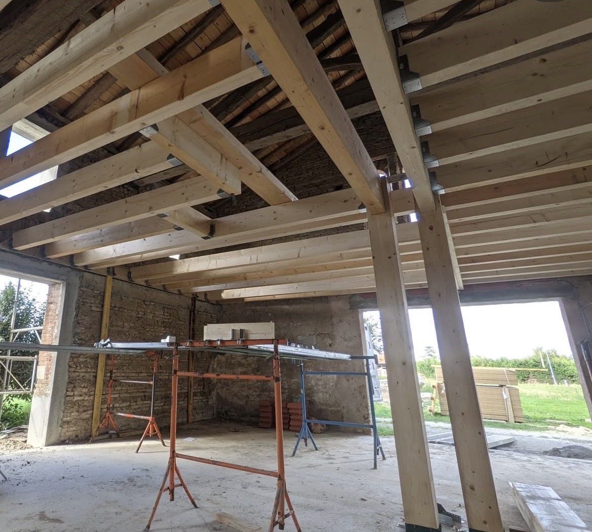 Charpente bois neuve dans une grange en rénovation avec murs de pierre et échafaudages.