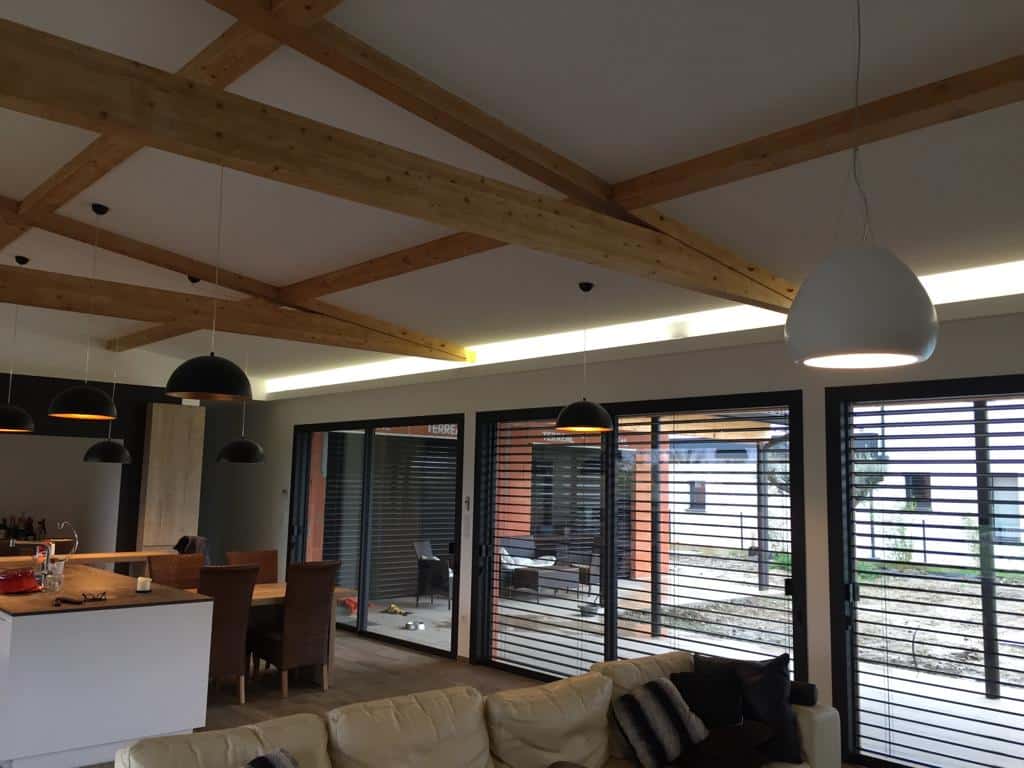 Intérieur moderne avec poutres en bois, luminaires design et grandes baies vitrées à stores horizontaux.