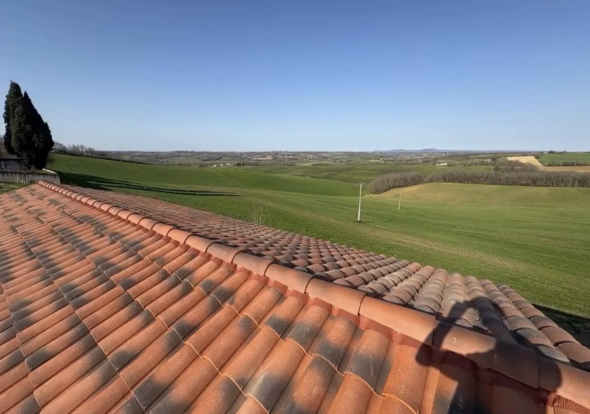 Toit en tuiles donnant sur des collines vertes sous un ciel bleu.