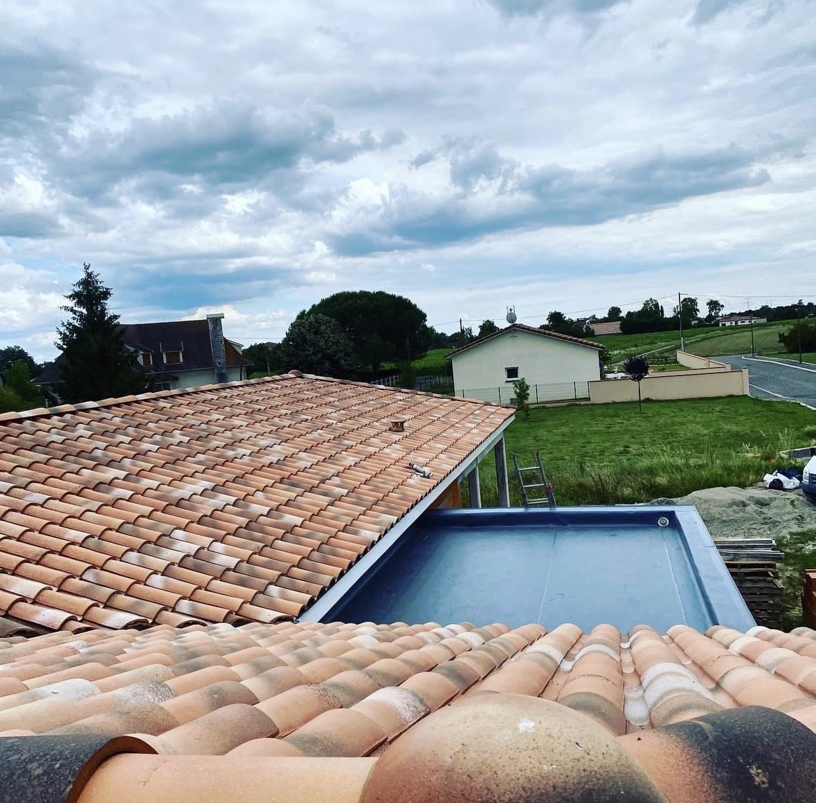 Toiture en tuiles terre cuite orange, extension toit plat et jardin sous un ciel nuageux.