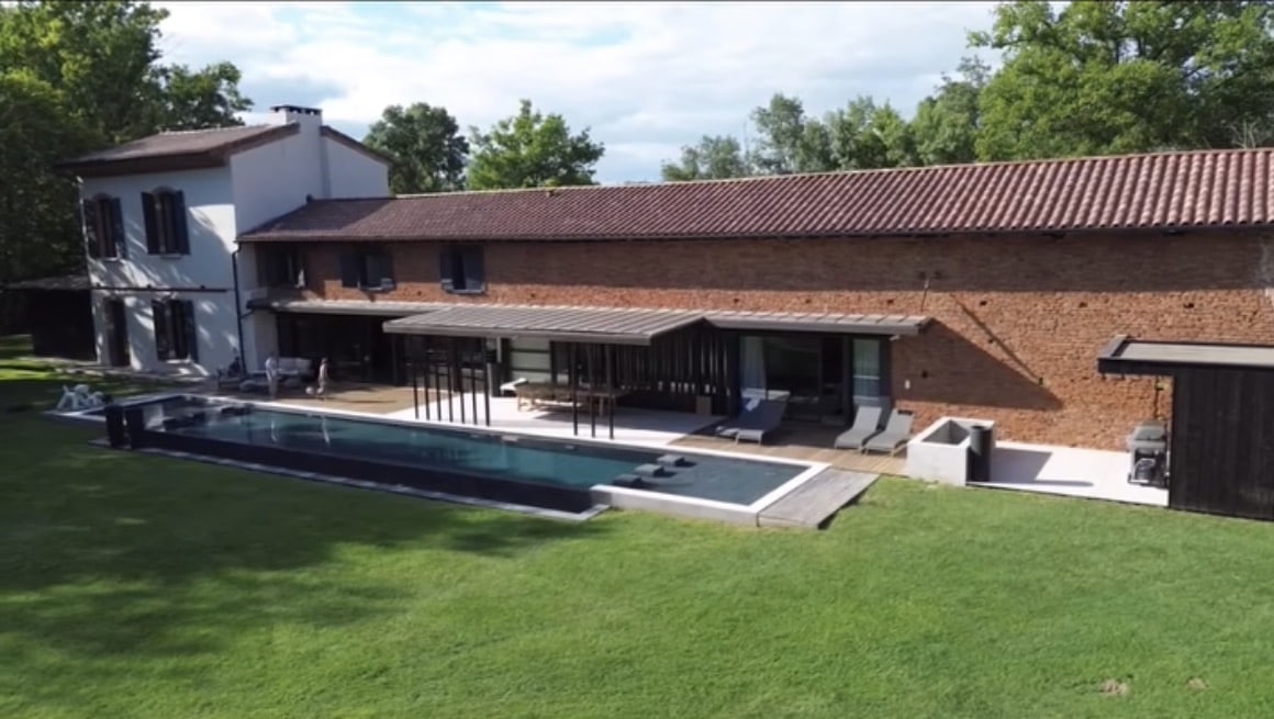 Ferme rénovée en briques, piscine miroir et terrasse moderne sur vaste pelouse.