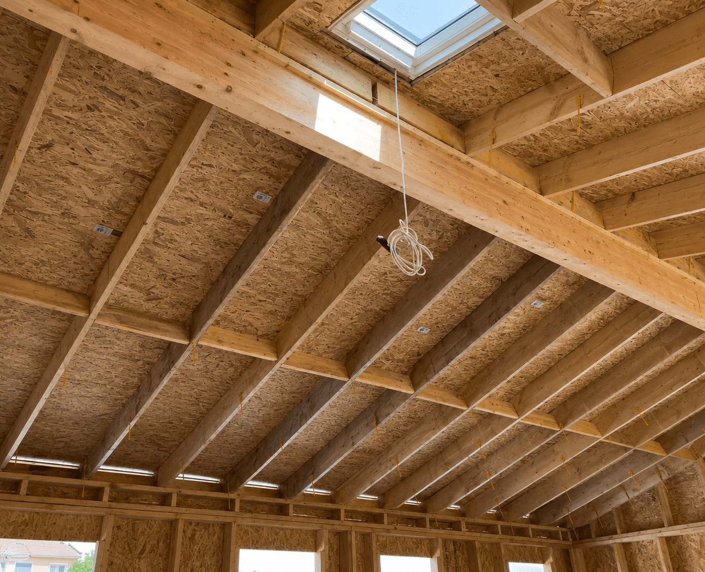 Charpente en bois apparente, panneaux OSB et puits de lumière d'une maison en construction.